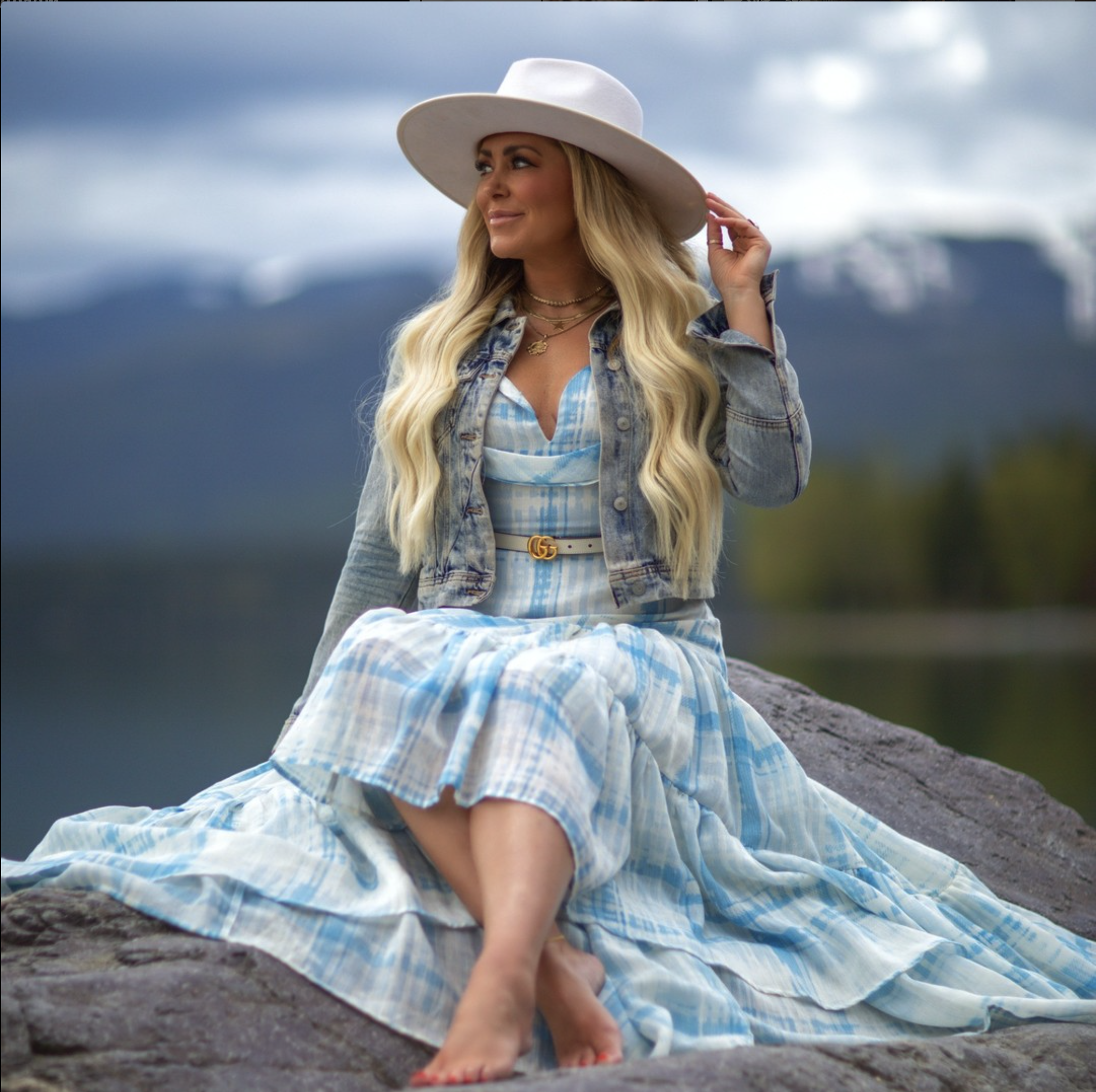 woman sitting on a rock with a twinstone cowboy hat in a blue dress